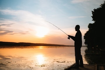 A fisherman silhouette fishing at sunset. Freshwater fishing, catch of fish