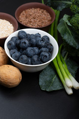 Mix of healthy vegetarian ingredients of vegetables, seeds, bran and berries on a black wooden background. Top view.