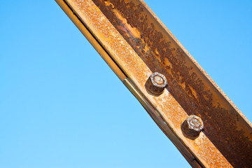 Old rusty iron structure with bolted metal profiles against a blue sky