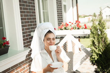 beautiful young brunette woman wearing dressing gown and white towel on her head enjoying cup of...
