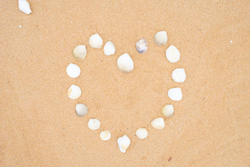 small seashells in the shape of a heart on a smooth sandy beach.