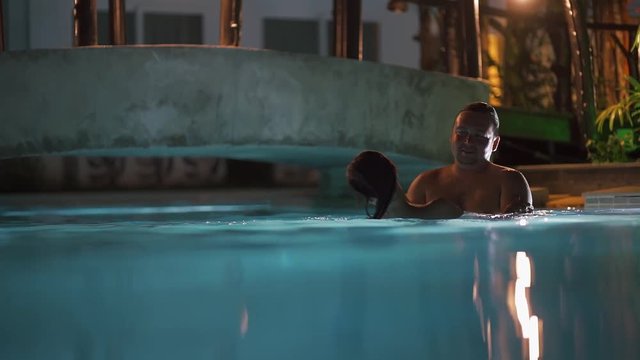 Young man and woman in the pool happily smiling, he turns her around.