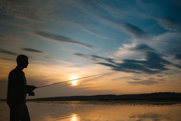 Fototapeta premium Fisherman at sunset on the river .Beautiful summer landscape with sunset on the river. Fishing. spinning at sunset. Silhouette of a fisherman