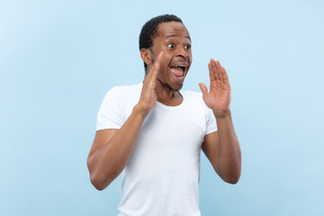 Half-length close up portrait of young african-american man in white shirt on blue background....