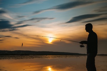 A fisherman silhouette fishing at sunset. Freshwater fishing, catch of fish