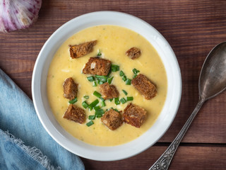 Cheese soup puree with crackers of dark bread removed from the top view, the head of young garlic and blue denim napkin on a wooden tray