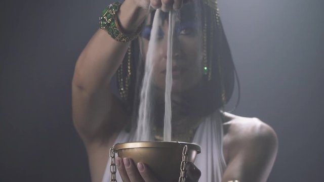 Slow motion footage of young Cleopatra pouring sand into the golden bowl