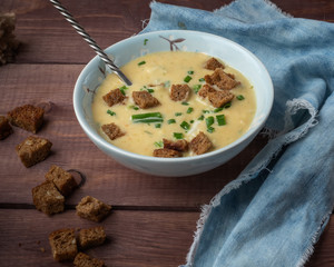 Fragrant vegetable soup mashed with cream and cheese in a deep blue plate with a spoon on a blue denim napkin, served on a wooden tray. Taken at close range, on a tray of dark bread crackers.