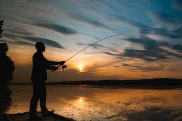 A fisherman silhouette fishing at sunset. Freshwater fishing, catch of fish