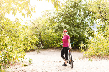 Bicycle teen with ladies bikes in summer park. Womens road bike for running on nature. Teenager girl in helmet cycling fording throught water. Girl carries weights on bicycle