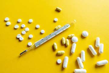 Thermometer, tablets, pills and other medicine scattered on a orange background. Treatment of illness, malaise. Close-up