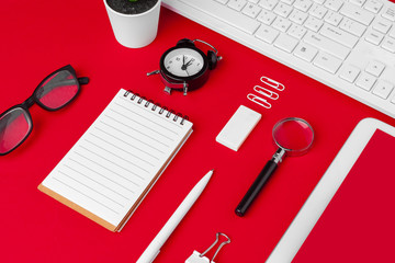 Red office desk table with blank notebook, keyboard and supplies. Top view with copy space. Flat lay.