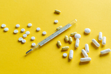 Thermometer, tablets, pills and other medicine scattered on a orange background. Treatment of illness, malaise.