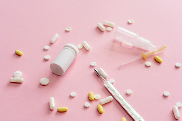 Thermometer and tablets, pills and other medicine scattered on a light pink background. Treatment of illness, malaise.