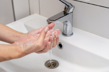 Women washing hands in the bathroom in the sink using purple color soap. Foam on hands