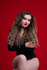 Beautiful, seductive woman posing in black bodysuit. Beauty photo. Wavy hair, perfect make up, hair developing in the wind. Afro curls hairstyle. Posing on the red background.