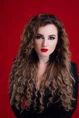 Hairstyle. Fashion girl with long curly hair, beauty makeup. Glamour portrait of beautiful brunette with red matte lips  isolated on red background.