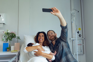 Couple taking selfie while holding their newborn baby in the ward