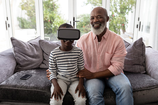 Grandson with grandfather using virtual reality headset in living room