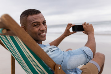 Man clicking pictures with mobile phone while sitting on a beach chair at beach