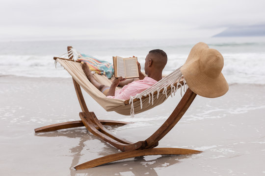 Man reading a book while relaxing on a hammock at beach