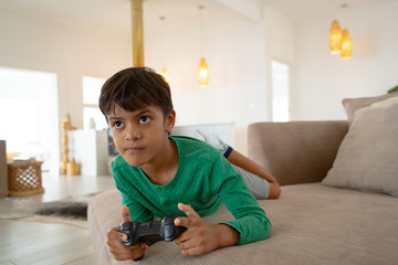Boy playing video game on sofa in living room at comfortable home