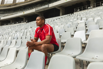 Thoughtful male rugby player sitting alone in stadium