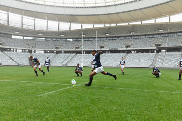 African American male rugby player kicking rugby ball in stadium.