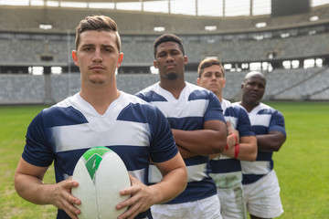 Male rugby players standing together with rugby ball in stadium
