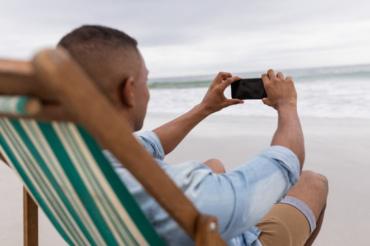 Man clicking pictures with mobile phone while sitting on a beach chair