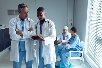 Male doctors discussing over digital tablet and female doctors using laptop