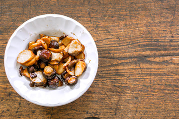 Fresh Shiitake Mushroom Stir Fried with Soy Sauce in Chinese style on white ceramic plate and wooden background. A Vegetarian food in Chinese Vegetarian Festival.