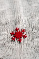 Beautiful light gray knitted pattern with red paper snowflake , knitted scarf close up. Knitted background, vertical
