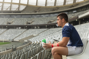 Caucasian male rugby player sitting with rugby ball in stadium