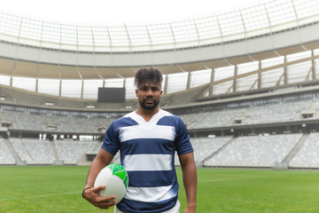 African American rugby player standing with rugby ball in stadium