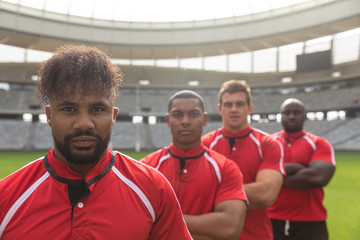 Male rugby players standing together with arms crossed in stadium