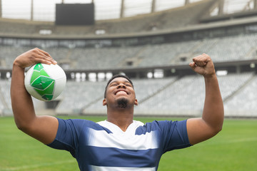 Happy African American Rugby player cheering with the ball in the stadium