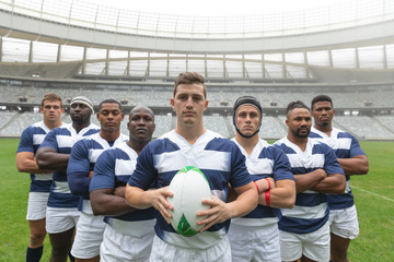 Group of diverse male rugby players standing together with rugby ball in stadium - Powered by Adobe