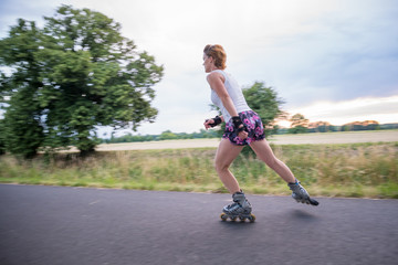 young woman rides on roller skates on an asphalt trail outside the city in summer