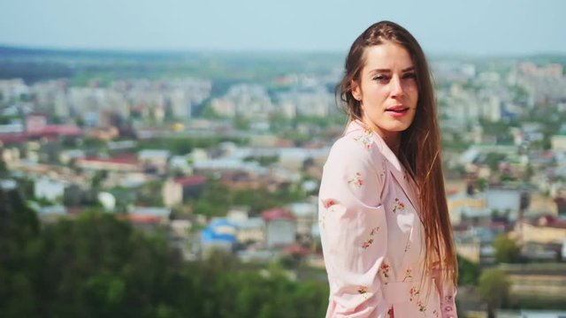 Gorgeous angel woman under sunlight against epic cityscape. Outdoor portrait of charming girl in pink dress enjoying freedom and life staying in highland nature over bit city. Happy life concept.
