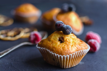Sweet muffins with berries on dark textured background.