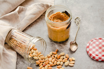 Fresh homemade creamy Peanut Butter in a glass jar on gray background