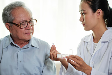 Fototapeta premium Asian young female doctor holding pills and explaining to her senior patient how to take the medicine during her visit