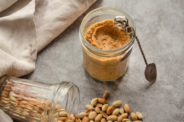 Fresh homemade creamy Peanut Butter in a glass jar on gray background.Comfort food concept.