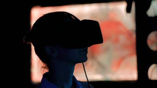 Woman using virtual reality headset and looking around at interactive technology exhibition with changing multi color light illumination. VR, augmented reality, immersive and entertainment concept