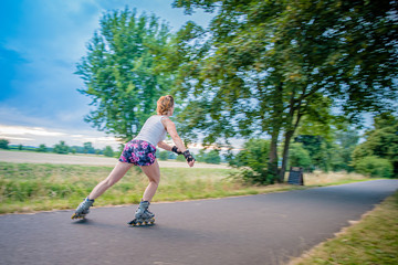 Fototapeta premium young woman rides on roller skates on an asphalt trail outside the city in summer