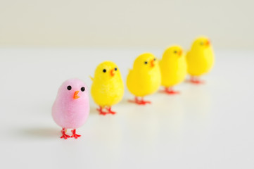 Small baby chicken toy of pink color and many chickens of yellow color on white table. Leadership or diversity concept