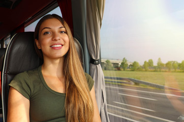 Smiling girl travelling in bus with the road out of the window looking at the camera