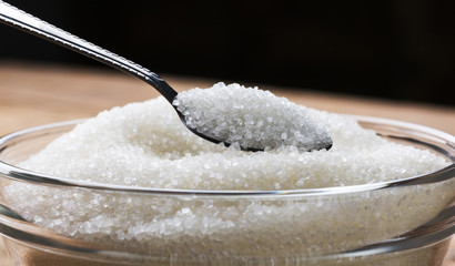 Sugar being poured from spoon into a bowl.  Bowl of sugar with spoon on wooden table