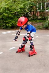 A small child in bright clothes, in a red helmet and protection goes on the road on rollers. Children's sport, active leisure.